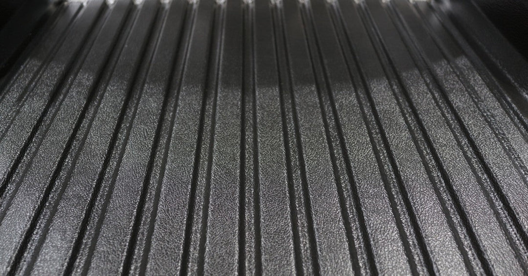 A close-up of the bed of a black pickup truck with a black plastic hard cover. The truck is parked in a parking lot.