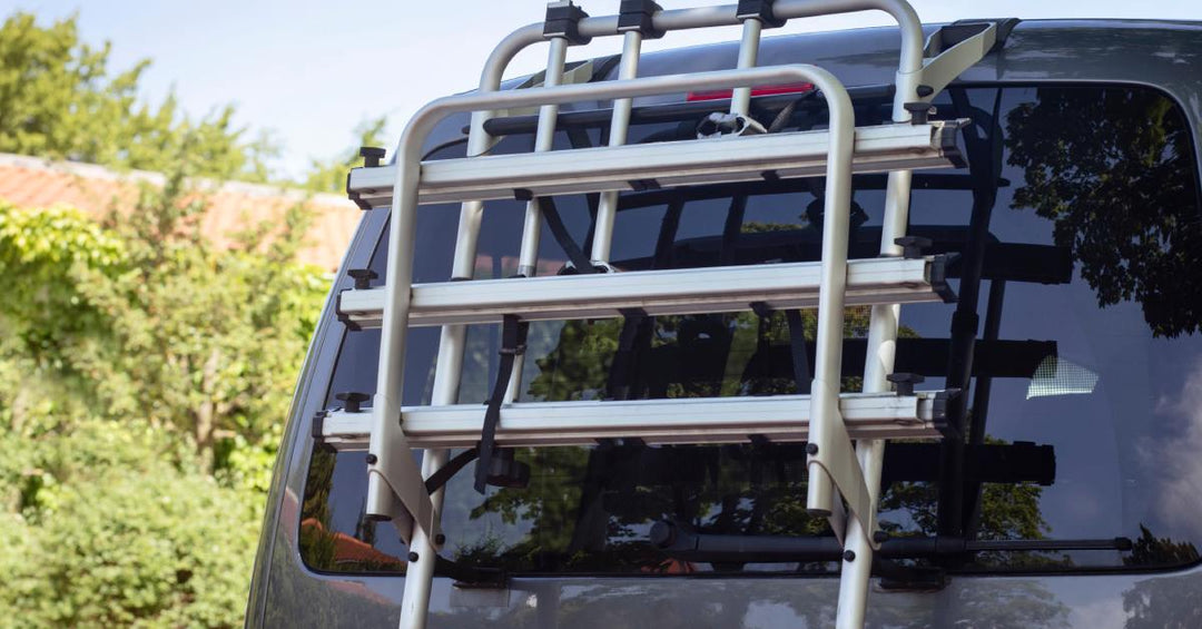 A close-up of the back of an SUV with a large white back rack covering the back windshield, parked next to a bush.