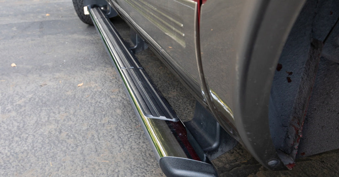 A close-up of a running board with an anti-slip rubber cover attached to the bottom of a grey pickup truck.