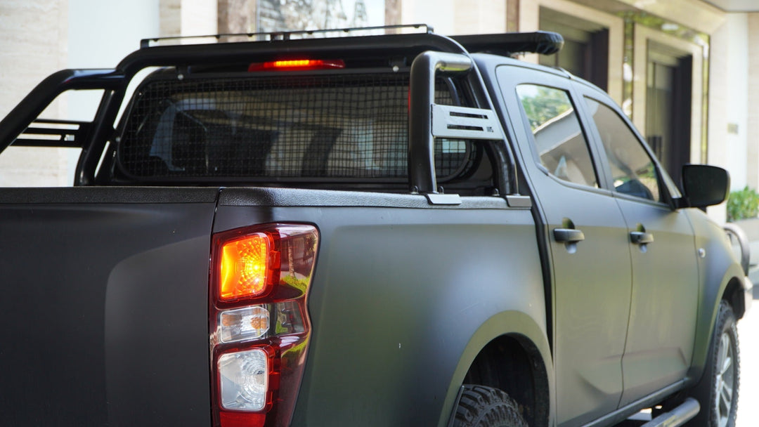 A black pickup truck with a headache rack on the back windshield parked in front of a home with taillights on.