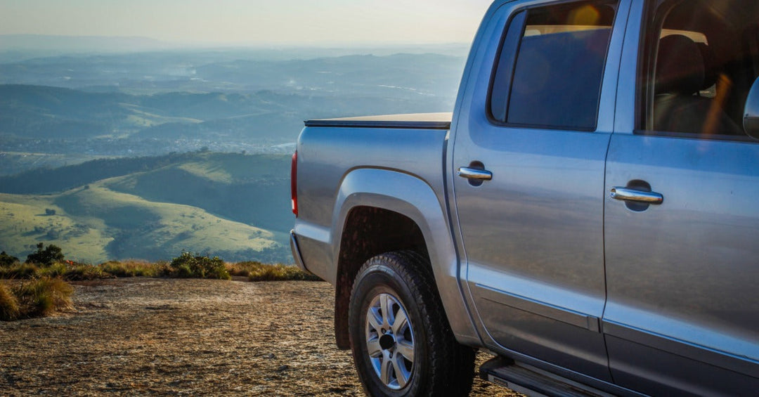 A grey pickup truck with a double cabin and a bed cover, parked on top of a hill overlooking a green landscape.