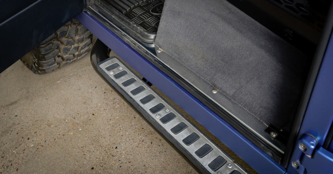 A close-up of a blue running board with multiple black squares attached to the side of a vehicle with large tires.