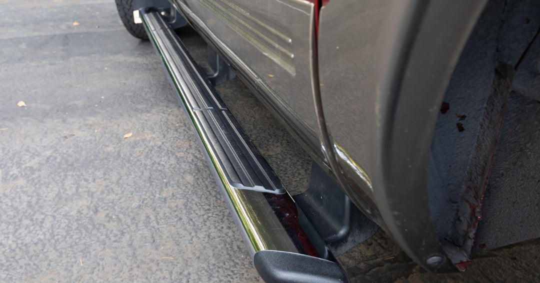 A close-up of a black running board with anti-slip details on the side of a red vehicle parked on a concrete surface.